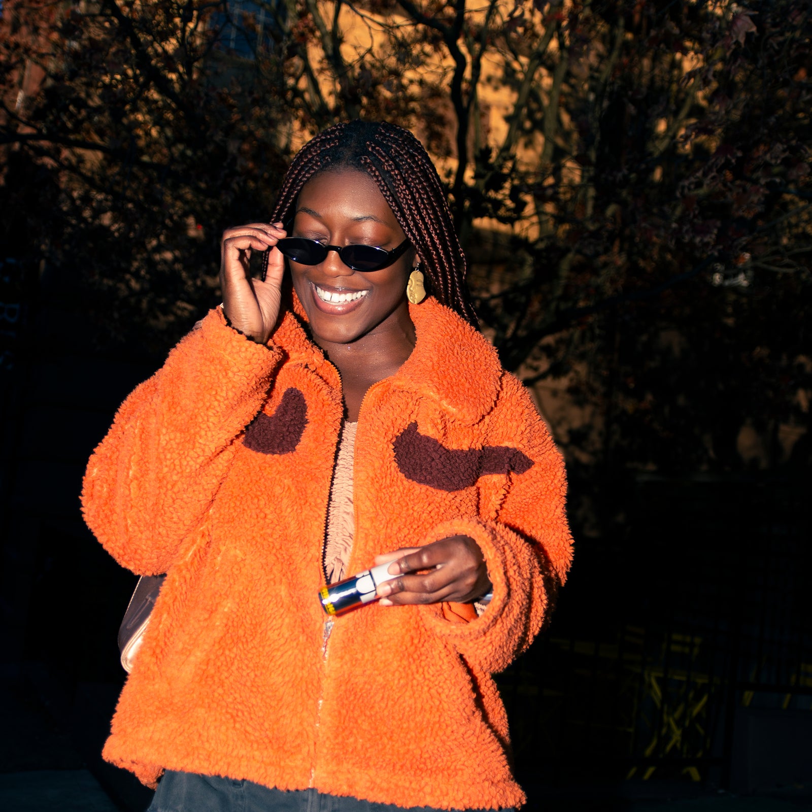 Person wearing an orange jacket with bird designs, standing outdoors with trees in the background.