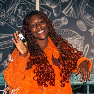 Woman in an orange sweater holding a phone with a colorful case against a chalkboard wall.