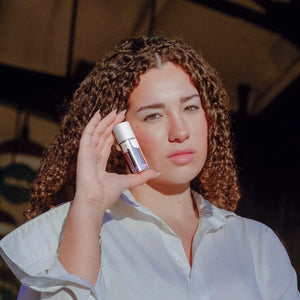 Woman holding a skincare product against her face outdoors